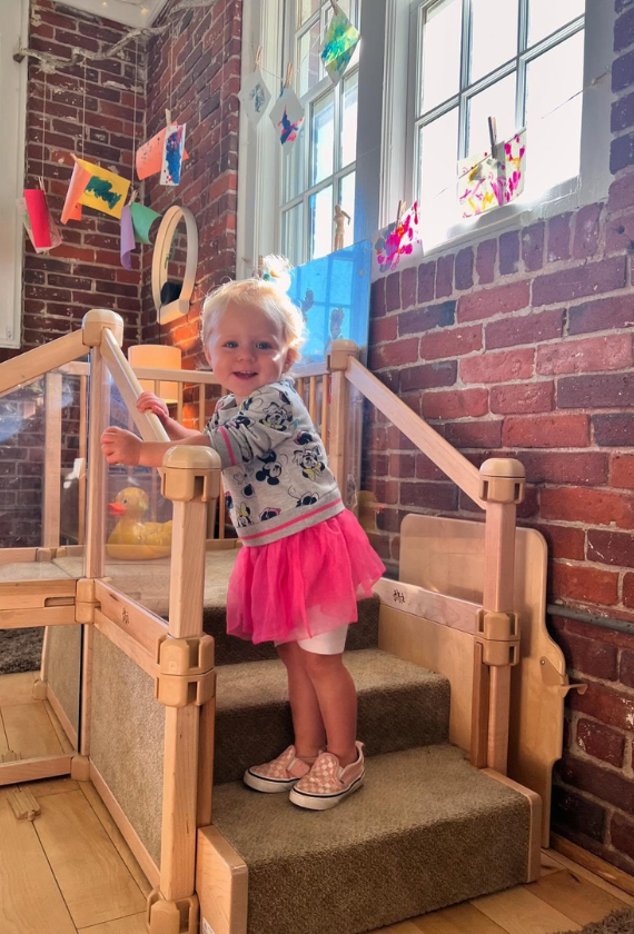 A toddler climbing the steps of a wooden classroom loft